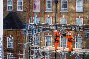 Two scaffolders working on a building site, wearing orange hi-vis protection clothes. Concept for construction workers, teamwork, work, infrastructure, building site, manual skills, lockdown.