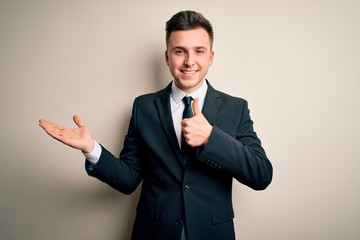 Young handsome business man wearing elegant suit and tie over isolated background Showing palm hand and doing ok gesture with thumbs up, smiling happy and cheerful