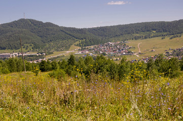 Suburb and villages. Big mountains and dark green forests far away. Trees and their shadows on the grass. Summer day with bright blue sky and huge white clouds on the landscape