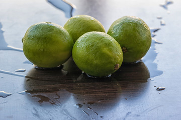 Four green fresh limes on a wet surface