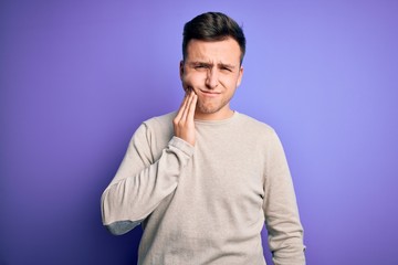 Fototapeta premium Young handsome caucasian man wearing casual sweater over purple isolated background touching mouth with hand with painful expression because of toothache or dental illness on teeth. Dentist