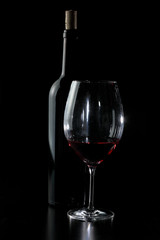 Bottle and glass of red wine with black background