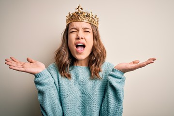 Young blonde girl wearing queen golden crown over isolated background celebrating mad and crazy for...