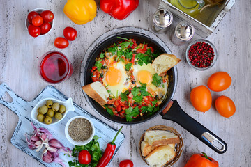 Fried eggs in a pan with vegetables and herbs, ripe tomatoes and peppers, zira, paprika, garlic, olives closeup. Delicious and nutritious breakfast. Country style