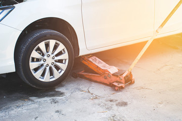 The orange hydraulic jack is lifting the sedan car in the auto repair shop,Automotive maintenance...