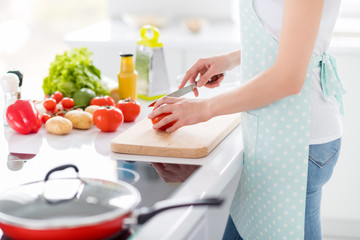 Cropped profile photo of housewife chef arms holding tomato cutting knife slices enjoy morning cooking tasty dinner family meeting wear apron t-shirt stand modern kitchen indoors
