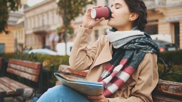 Attractive young woman is drinking hot beverage, while sitting on the bench. Close up. Copy space. 4K.