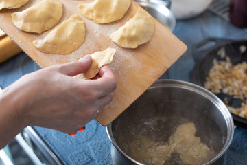 cooking dumplings with potatoes, a woman takes a dumpling from a wooden board and throws it into a pot of boiling water, Russian cuisine