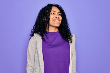 Young african american sporty woman wearing casual sweatshirt over purple background looking away to side with smile on face, natural expression. Laughing confident.