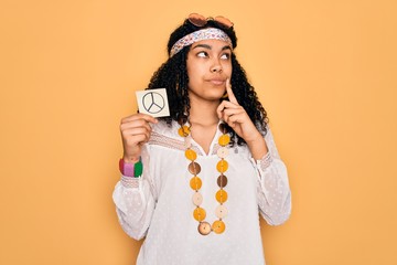 African american curly hippie woman wearing sunglasses holding reminder with peace symbol serious face thinking about question, very confused idea