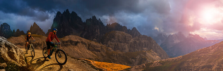 Cycling outdoor adventure in Dolomites. Cycling woman and man  on electric mountain bikes in Dolomites landscape. Couple cycling MTB enduro trail track. Outdoor sport activity.
