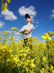 chłopczyk w czapeczce i w okularach stojący w polu kwitnącego rzepaku  - obrazy, fototapety, plakaty