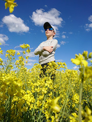 chłopczyk w czapeczce i w okularach stojący w polu kwitnącego rzepaku 