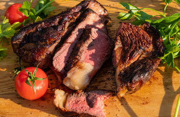 Сooked and sliced ​​beef steak with tomatoes and greens on a wooden cutting board