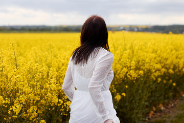 Fototapeta premium Young woman in a white dress is running along rapeseed field. Concepts of success, ecology and freedom with copy space.
