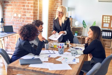 Group of business workers smiling happy and confident. Working together with smile on face. Middle age beautiful woman standing explaining documents at the office