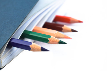 Five different colored wood pencil crayons placed in a white paper notebook