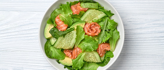 Salmon salad, cucumber, spinach, lollo, lettuce. Homemade vegetarian salmon salad. Seafood creative diet concept. Summer salmon salad on white wood, closeup, banner