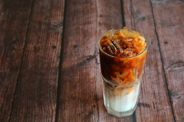 A glass of iced milk with espresso shot on top. Iced coffee on wooden table have copy space at left area.