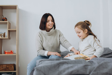 Pretty young mother reading a book to her daughter. Family holiday and togetherness.