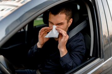 young man with handkerchief. Sick guy has runny nose. Male model makes a cure for the common cold in the car.