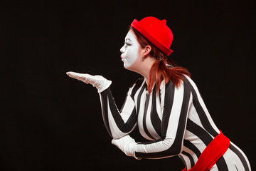 Portrait of female mime artist performing, isolated on black background. Woman blows a kiss posing...