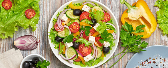 Fototapeta na wymiar Greek salad with cucumeber, olives, feta cheese, cherry tomatoes, bell pepper and lettuce. Summer diet salad concept. Tasty greek salad in bowl on wood, top view, banner