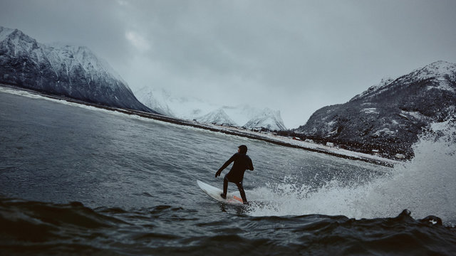 Surfer rides wave in bay surrounded by snowy mountains