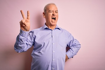Fototapeta premium Middle age handsome hoary man wearing casual shirt standing over pink background smiling with happy face winking at the camera doing victory sign. Number two.