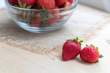 Strawberries in a glass plate on a wooden background. Strawberry season.