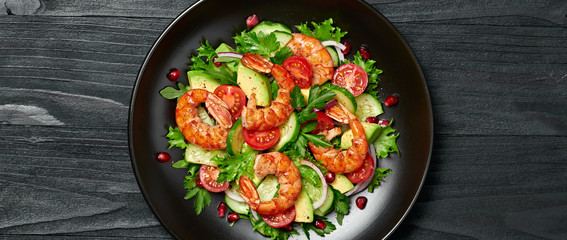 Shrimps salad, avocado, lettuce, cherry tomatoes. Homemade vegetarian shrimp salad. Seafood concept. Mixed leaves, grilled prawn shrimps in plate on black wood background, banner