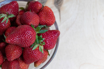Strawberries in a glass plate on a wooden background. Strawberry season.