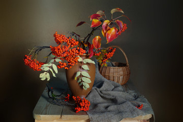Still life with red Rowan in a vase on a table on a brown background.