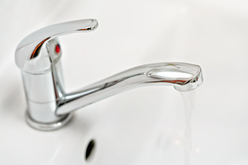 Chrome tap faucet with water flowing, blurred bathroom background