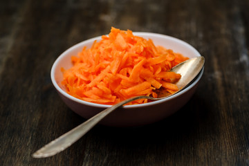 Raw grated carrot on a wood table with a spoon