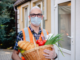 Portrait of a male volunteer in a medical mask near the front door with a basket full of food.