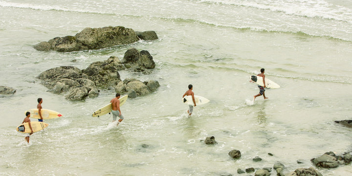 Cinco amigos surfistas carregando pranchas na praia em dire&ccedil;&atilde;o ao mar. Vis&atilde;o a&eacute;rea.