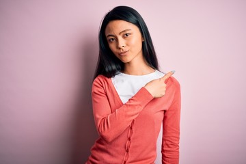Fototapeta premium Young beautiful chinese woman wearing casual sweater over isolated pink background Pointing with hand finger to the side showing advertisement, serious and calm face