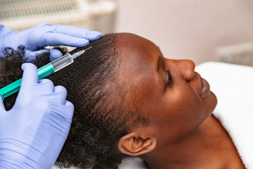 Doctor aesthetician makes head beauty injections to a female african patient