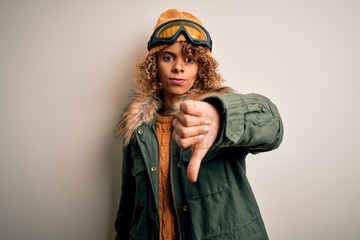Young african american skier woman with curly hair wearing snow sportswear and ski goggles looking unhappy and angry showing rejection and negative with thumbs down gesture. Bad expression.