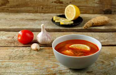 Tom yum soup with chicken in a plate on a tablecloth on a linen napkin next to garlic and lemon.