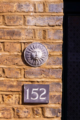 House number 152 on a brick wall under a round  ornament showing a stylised sun