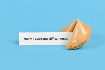 Fortune cookie with motivational text on paper saying 'You will overcome difficult times' on blue...