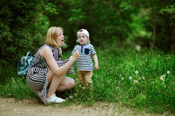 Fototapeta premium mother with a small son opening his mouth to blow on a flowering dandelion in a green juicy meadow
