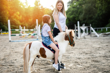 Cute little girl and her older sister enjoying with pony horse outdoors at ranch.