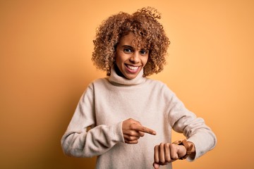 Young beautiful african american woman wearing turtleneck sweater over yellow background In hurry...