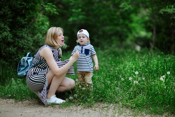 young beautiful mother with a small son, frozen from admiration and anticipation, opening his mouth to blow on a flowering dandelion in a green juicy meadow