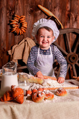 A young child in a chef's apron and hat plays the role of a baker.
The table is full of clutter. The mood is sublime. There are many ingredients and 
different things around. Concept for bakery.