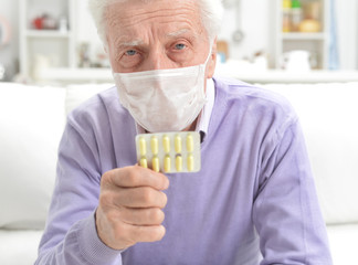 Portrait of sad sick senior man with facial mask holding pills