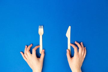 Top view and flat lay of bamboo wooden cutlery isolated on blue background. Female hands holding fork and knife. Zero waste concept. No plastic. Flat lay banner, top view, Sustainable lifestyle